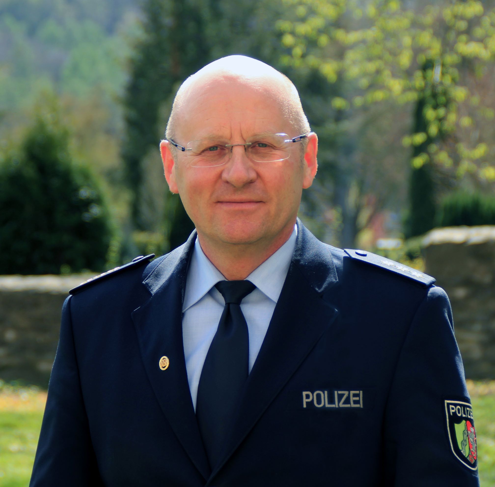 Abteilungsleiter der Polizei Siegen-Wittgenstein Klaus Bunse in Polizeiuniform. Er steht im Vordergrund. Hinten ist eine parkähnliche Landschaft zu sehen.