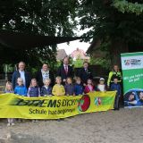 Kindergartenkinder hinter einem gelben Bann der Verkehrswacht mit der Aufschrift Brems dich! Schule hat begonnen.