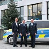 Auf dem Bild sind drei Personen abgebildet, die vor einem Streifenwagen und einem Weihnachtsbaum stehen.