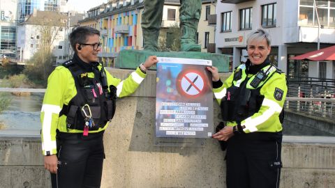 Zwei Polizeibeamtinnen präsentieren das Plakat zur Kampagne Besser ohne Messer auf der Siegener Siegbrücke