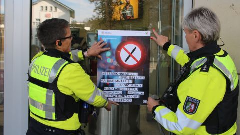 Das Kampagnenplakat Besser ohne Messer wird am Eingang des SiegCarre durch zwei Polizeibeamtinnen aufgehangen