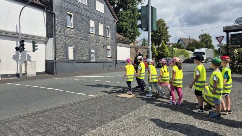 Polizeibeamtin übt mit Vorschulkindern das sichere Überqueren der Straße an einer Fußgängerampel