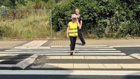 Eine Polizeibeamtin trainiert mit einem Kind das sichere Überqueren der Straße an einem Zebrastreifen.