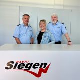 Die drei Protagonisten der Sendung stehen hinter einem Tresen mit dem Schriftzug Radio Siegen.